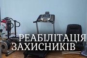 Кімната з різноманітним реабілітаційним тренажерним обладнанням, включаючи бігову доріжку, еліптичний тренажер та інші фітнес-пристрої, з текстом "РЕАБІЛІТАЦІЯ ЗАХИСНИКІВ", накладеним на зображення.