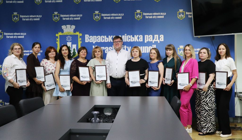 Колективне фото працівників бухгалтерської сфери Вараської громади спільно з міським головою м.Вараш Олександром Мензулом. Позаду людей синій банер з логотипом "Вараська міська рада Varash city council"