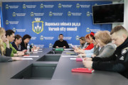 На фотографії інтер'єр приміщення, де відбувається зустріч. За столами сидять люди, а на задньому плані видно банер з написом: "Вараська міська рада"