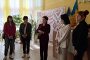 П’ятеро жінок стоять у приміщенні Вараського міського центру реабілітації під час заходу до Національного тижня безбар’єрності. Позаду – декоративна панель із вишитим орнаментом та державні прапори України. У кімнаті багато зелених рослин, тепле світло від жовтих штор. Усі учасниці уважно слухають виступ однієї з жінок.