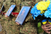 У День Героїв вояки тримають портрети загиблих побратимів — тих, хто віддав своє життя за Україну. Поруч — ордени «За мужність» III ступеня, якими держава відзначила наших захисників посмертно. Жовто-блакитні квіти в руках — символ вдячності й нескінченної памʼяті.